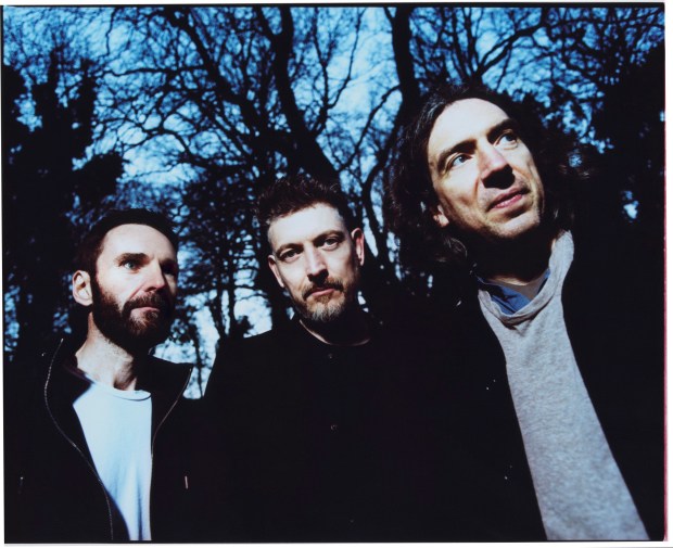 three men standing next to each other with trees in the background