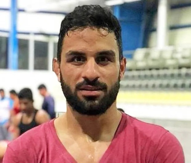 a man with a beard is wearing a pink shirt and looking at the camera .