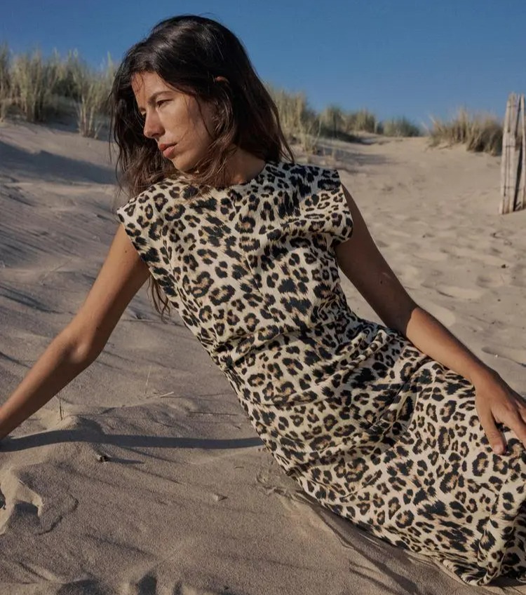 a woman in a leopard print dress is laying in the sand