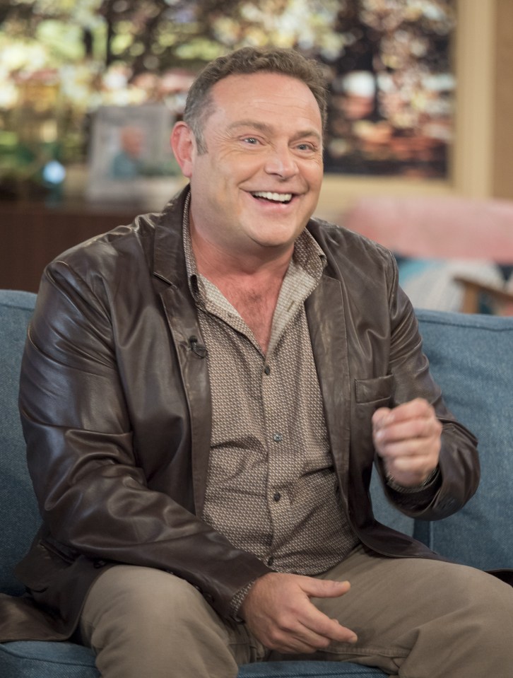 a man in a leather jacket is sitting on a couch and smiling