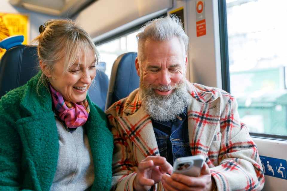 a man and a woman sitting on a bus looking at a cell phone