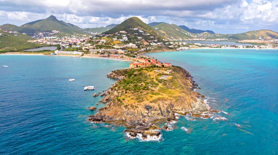 a small island in the middle of the ocean with mountains in the background