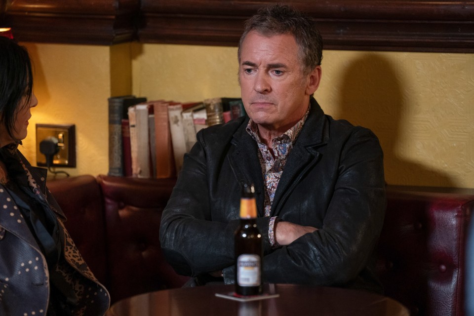 a man in a leather jacket sits at a table with his arms crossed