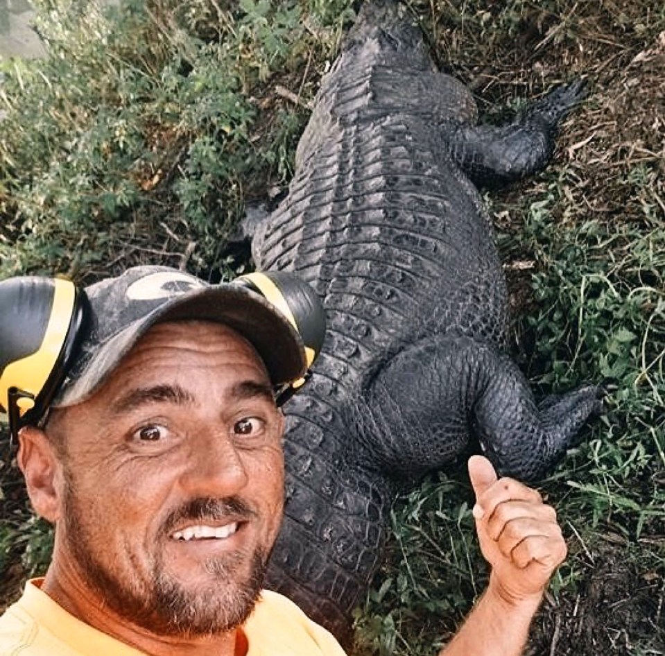 a man is standing next to a large alligator and giving a thumbs up