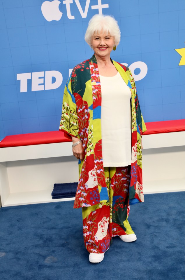 a woman wearing a colorful kimono stands on a blue carpet with the word ted on it