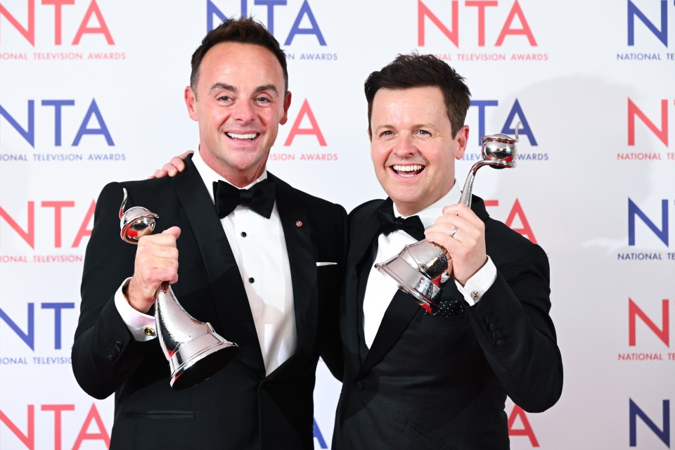 two men holding trophies in front of a wall that says national television awards