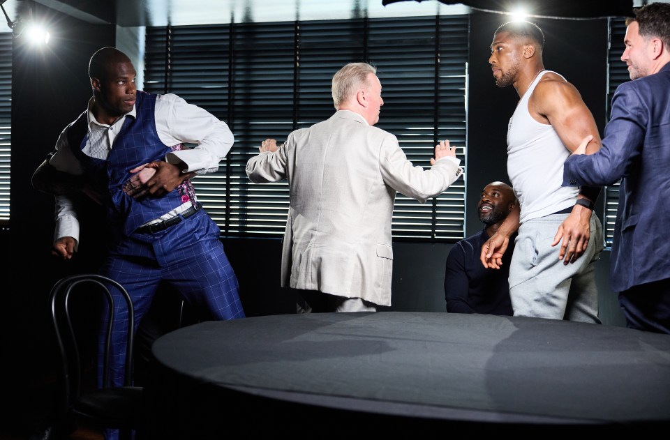 a group of men are standing around a table and one of them is wearing a white tank top