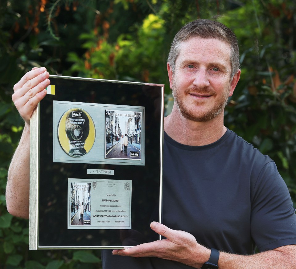 a man is holding a framed oasis album