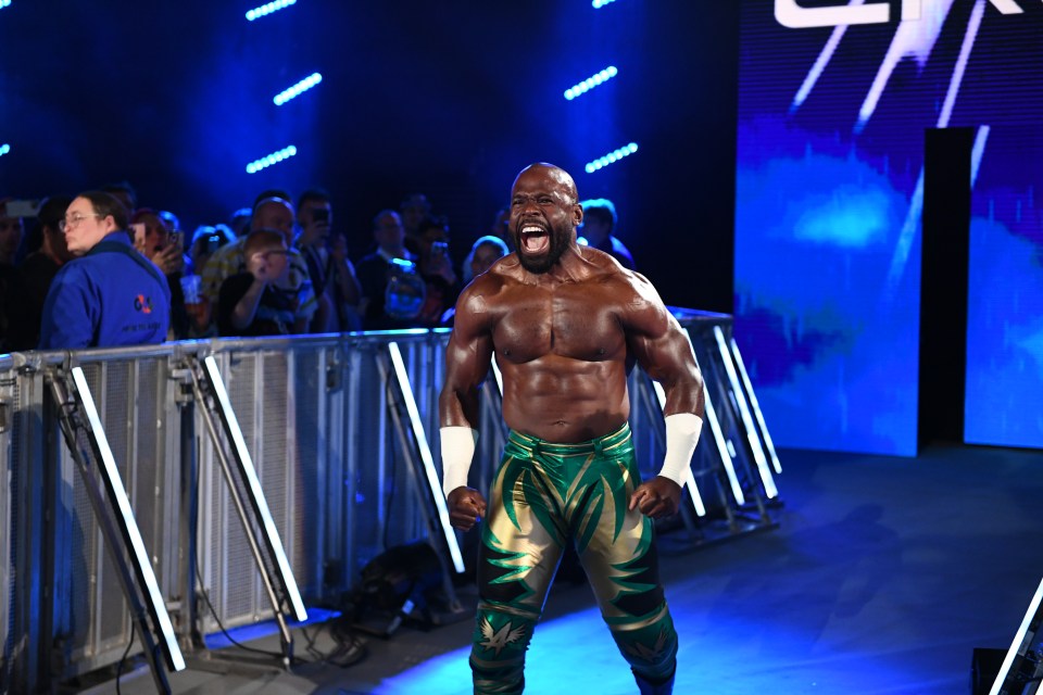 a wrestler in green and gold pants stands in front of a crowd