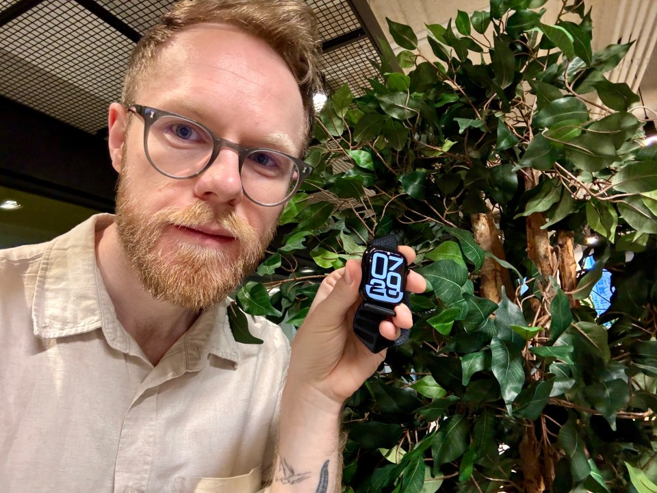 a man wearing glasses holds up a smart watch that shows the time as 10:29