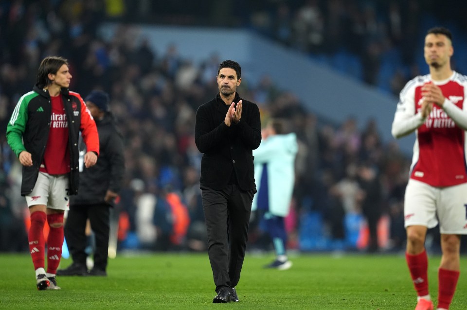 a man in a black jacket applauds on a soccer field