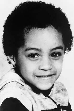 a young boy with curly hair is smiling in a black and white photo .