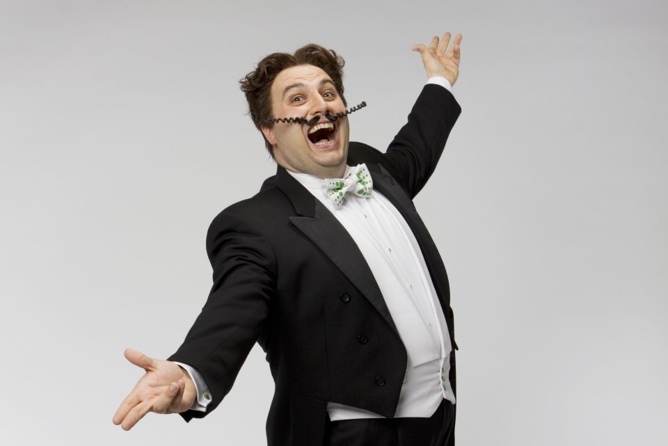 a man in a tuxedo and bow tie has his arms outstretched