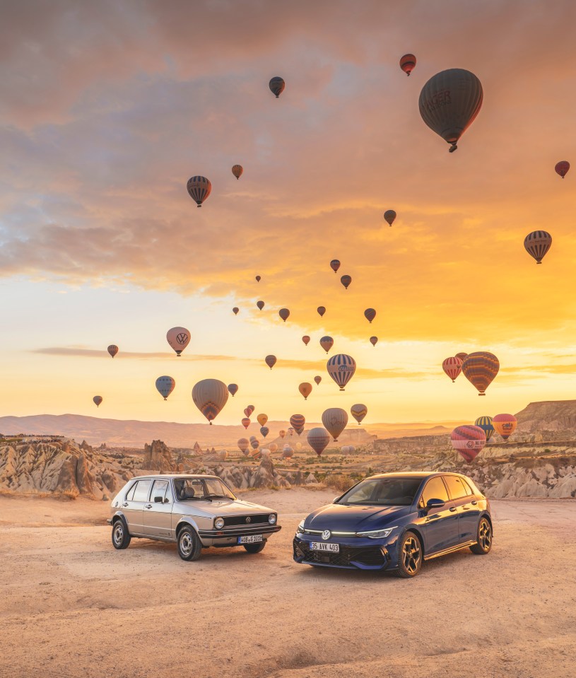 two cars are parked in a desert with hot air balloons in the background