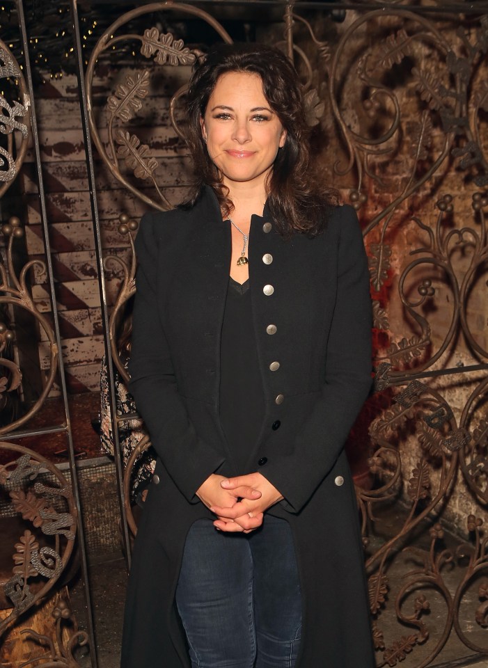 a woman in a black coat stands in front of a wrought iron fence