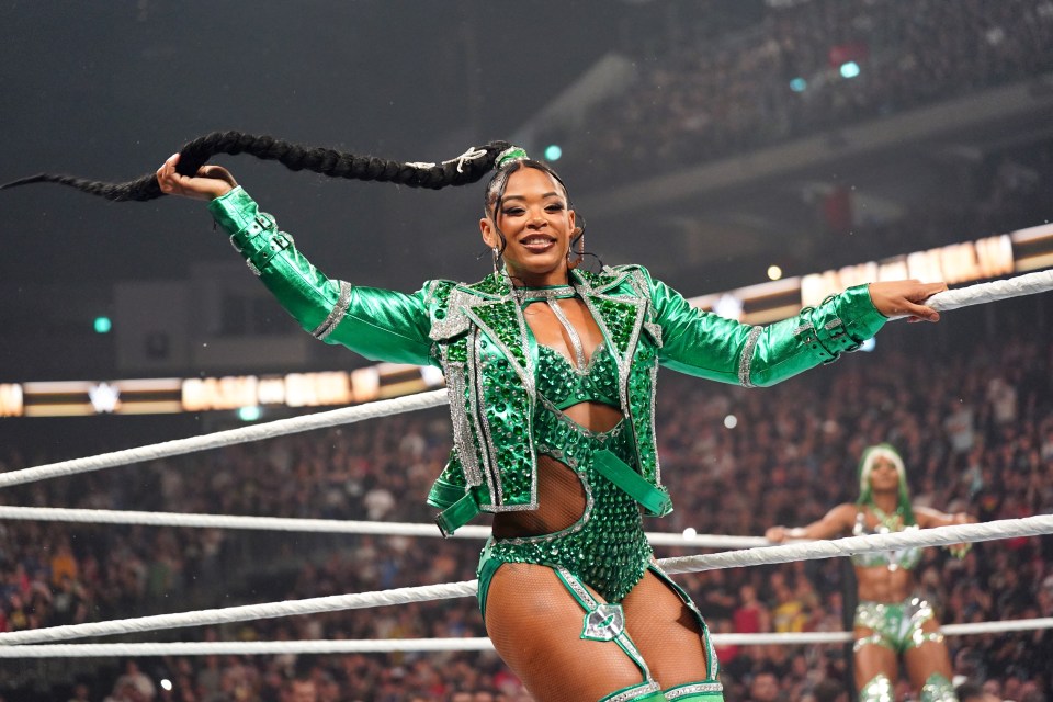 a woman in a green outfit stands in a wrestling ring