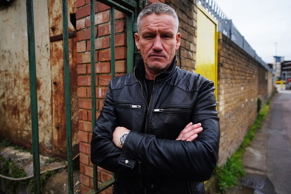 a man in a black leather jacket stands with his arms crossed