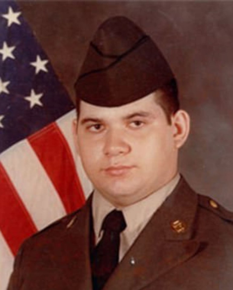 a man in a military uniform stands in front of an american flag