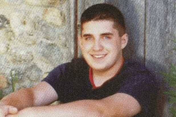 a young man is sitting in front of a wooden wall and smiling .