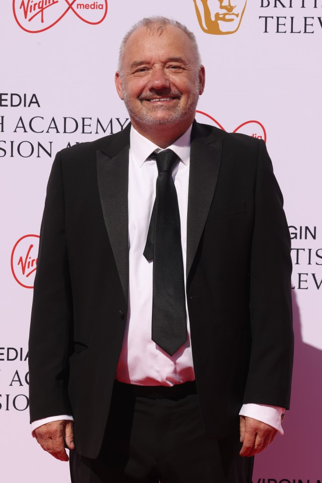 a man in a suit and tie stands in front of a virgin media logo