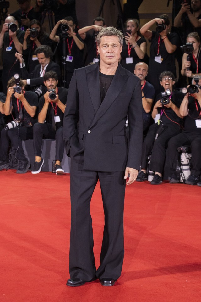 a man in a black suit stands on a red carpet