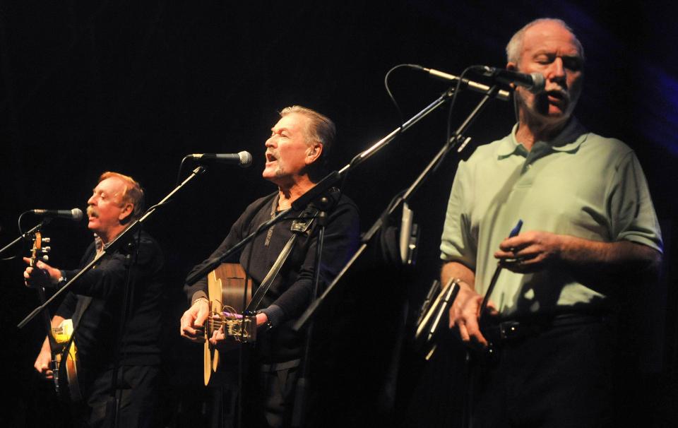 three men singing into microphones while playing instruments