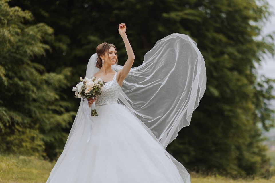 a woman in a wedding dress with her veil blowing in the wind