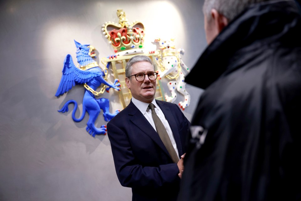 a man in a suit talks to another man in front of a coat of arms