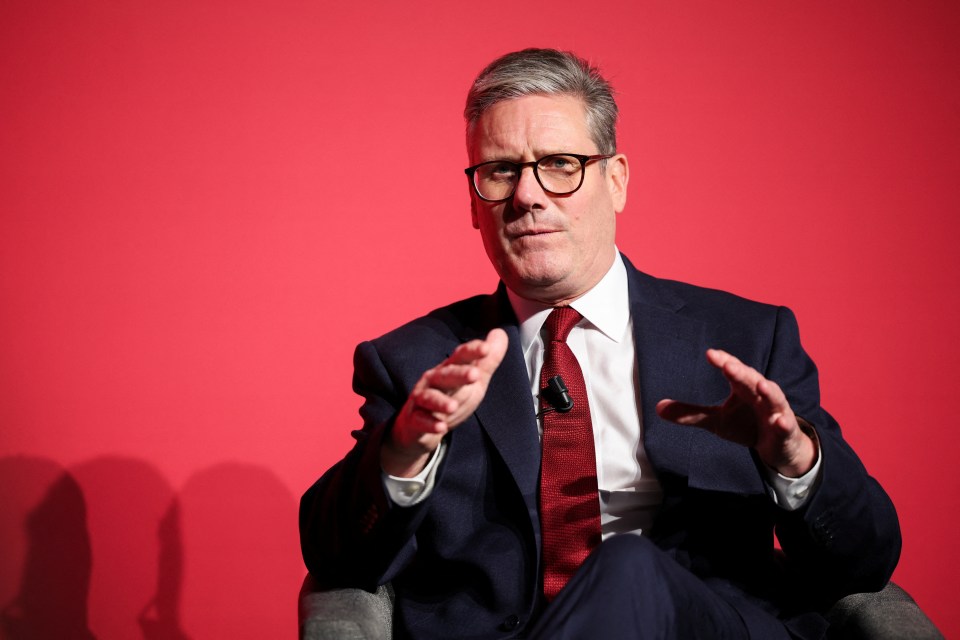 a man in a suit and tie is sitting in front of a red wall