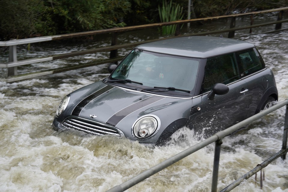 a gray mini cooper is driving through a flooded area