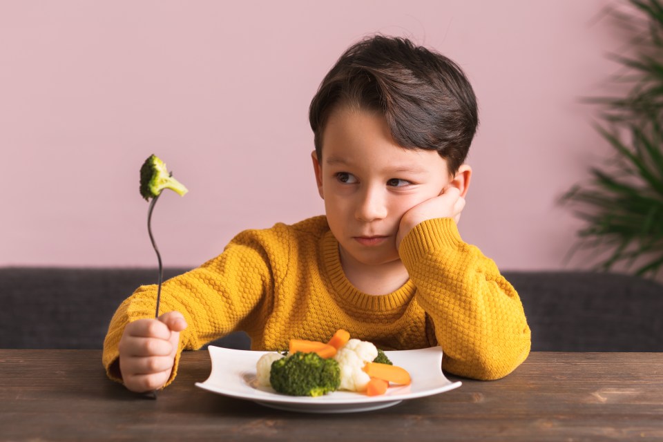 a young boy is holding a fork in front of a plate of vegetables