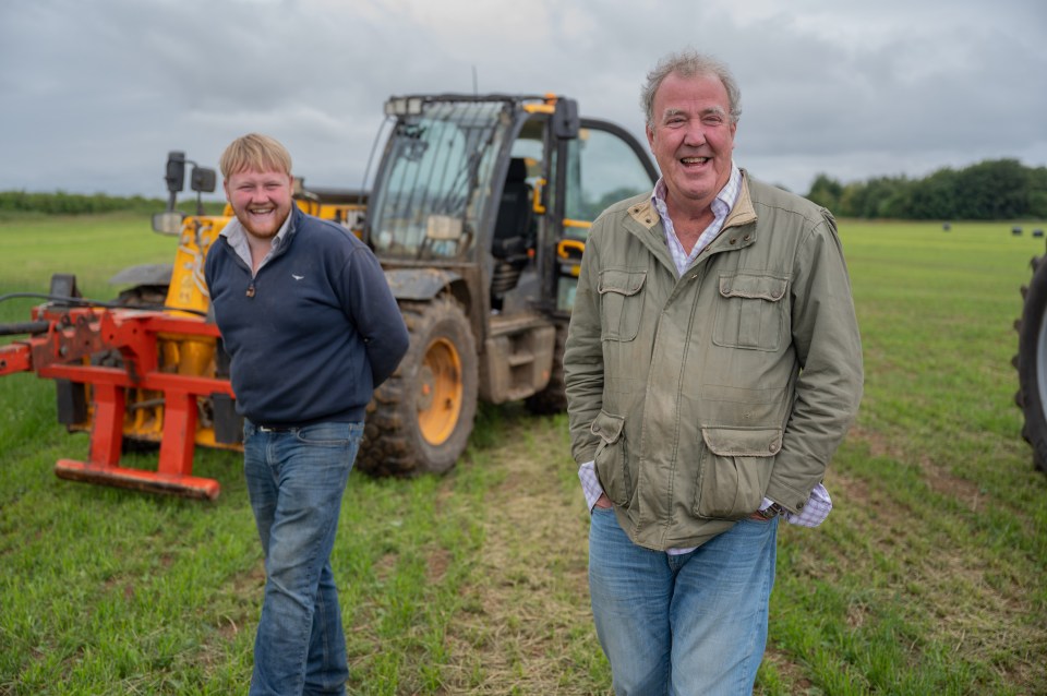 two men standing in a field with a tractor in the background