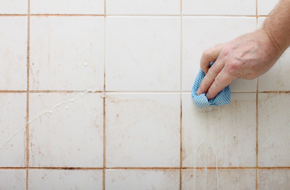 a person cleaning a tile wall with a blue and white cloth