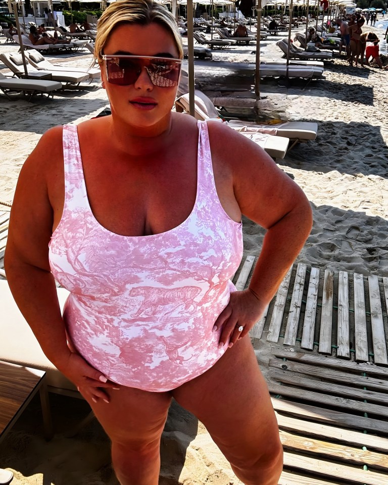 a woman in a pink swimsuit and sunglasses stands on a beach