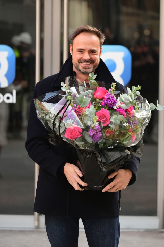 a man holding a bouquet of flowers in front of a building with the letter b on it