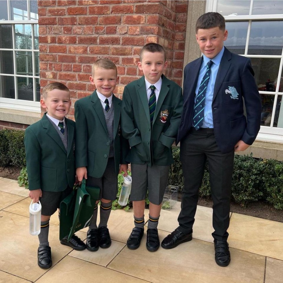 four boys in school uniforms stand in front of a brick building