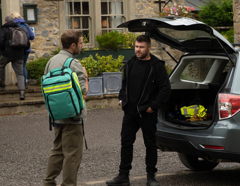 two men standing next to a car with the trunk open