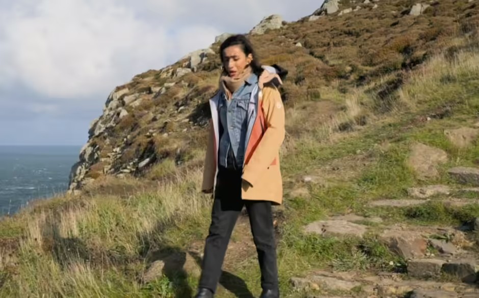 a woman is standing on a rocky hill near the ocean