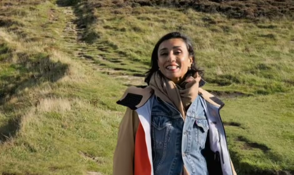 a woman in a denim jacket and scarf is standing in a grassy field .