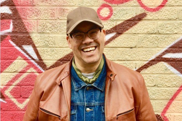 a man wearing glasses and a hat is smiling in front of a brick wall