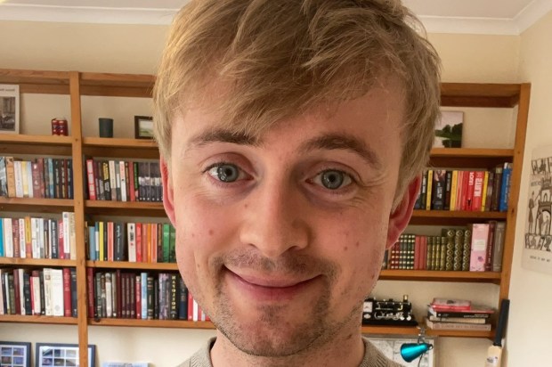 a man in a grey sweater is smiling in front of a bookshelf