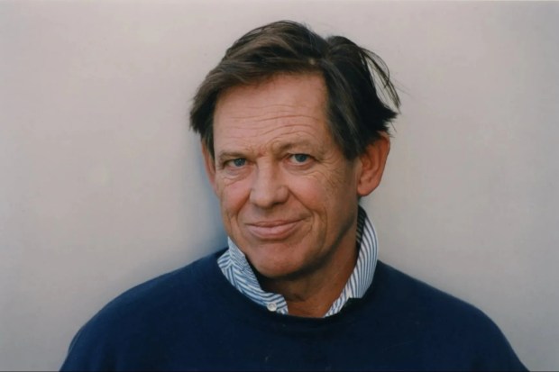 a man wearing a blue sweater and striped shirt looks at the camera