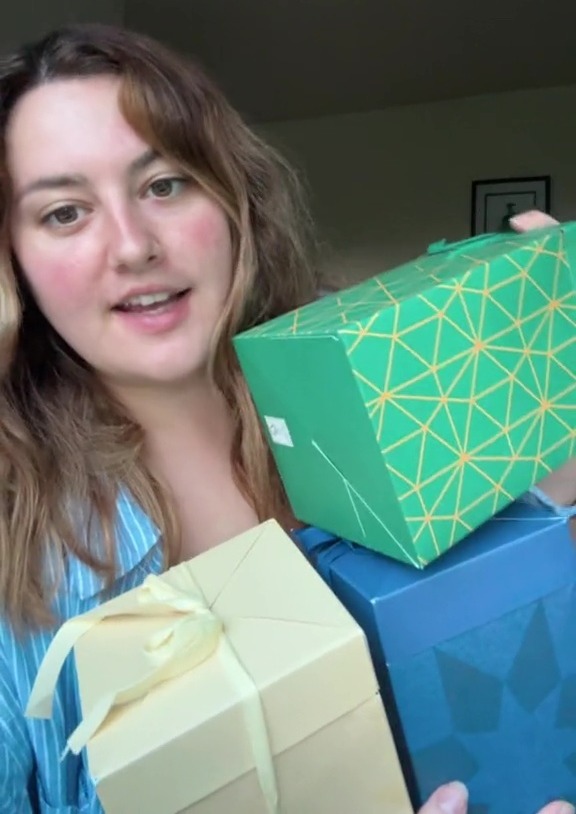 a woman is holding a stack of gift boxes including one that says ' a ' on it