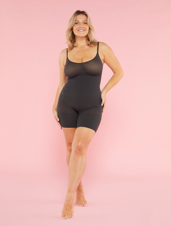 a woman in a black bodysuit is standing on a pink background