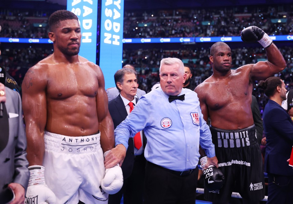 anthony joshua stands next to a referee in a boxing ring