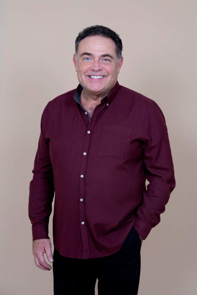 a man in a maroon shirt is smiling with his hands in his pockets