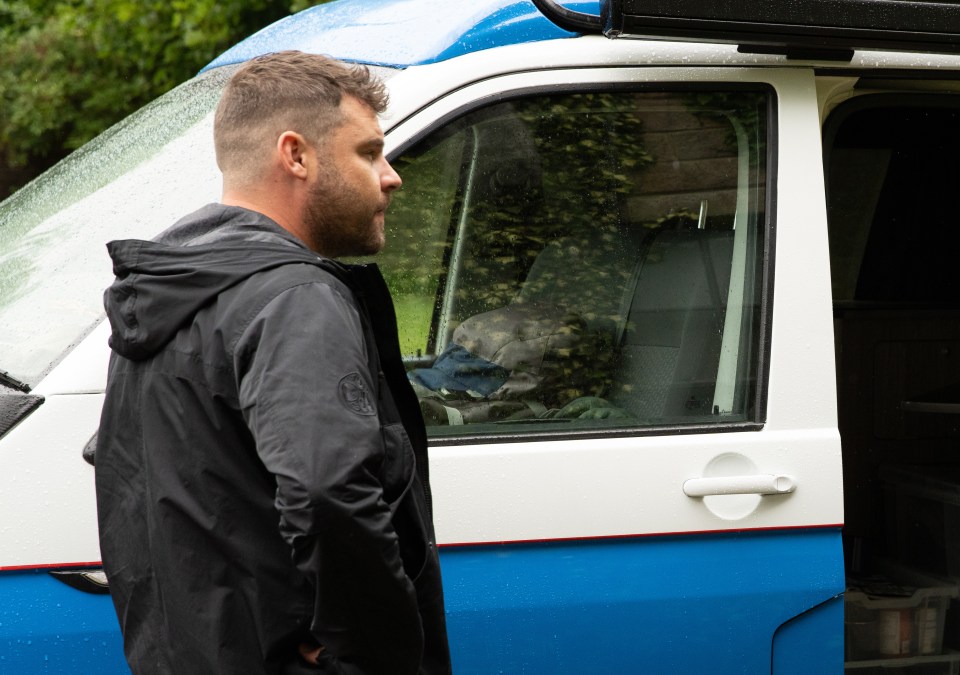 a man in a black jacket stands in front of a blue and white van