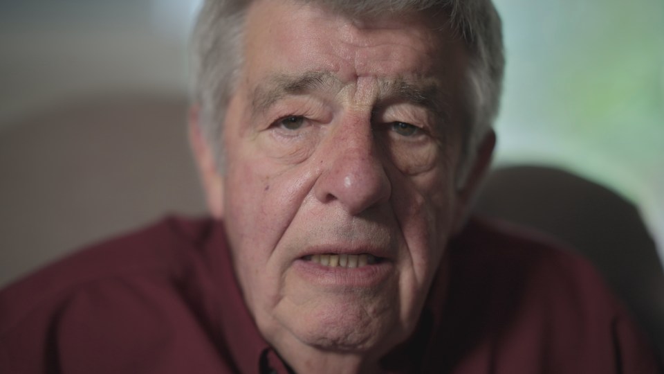 a close up of an older man 's face with a red shirt on