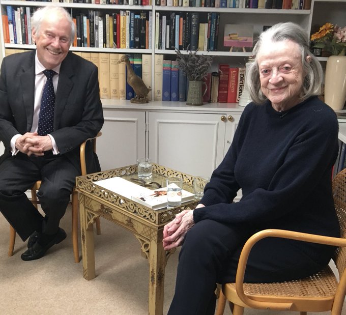 a man and woman sit at a table with a dictionary on the shelf behind them