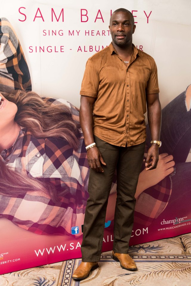 a man stands in front of a poster for sam bailey sing my heart single album